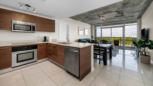 A modern kitchen with a central island, stainless steel appliances, and a large window overlooking a balcony.