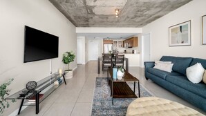 A modern living room with a flat-screen TV, a sofa, a coffee table, and a dining area with chairs and a table.
