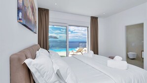Hotellihuone, jossa on suuri sänky, taulu seinällä ja merinäköala ikkunasta.