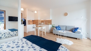 A modern, well-lit apartment with a kitchen, dining area, and a living room with a sofa and a TV. - Baltico Studio Apartment (Gdansk)