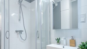 A modern bathroom with a glass-enclosed shower, a white sink with a wooden countertop, and a mirror above the sink. - Baltico Studio Apartment (Gdansk)