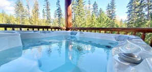 Un bain à remous avec une terrasse en bois et une forêt en arrière-plan.