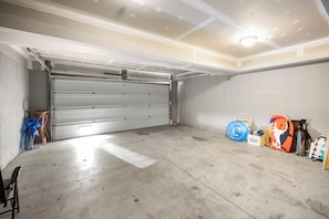Un garaje con puerta cerrada, piso de concreto y varios objetos como una llanta azul, una tabla de surf y un trípode.