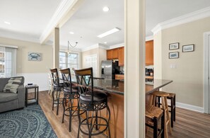 Una cocina moderna con una isla central, taburetes de bar y un área de comedor con sofá y alfombra.