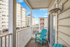 Ein Balkon mit Blick auf mehrstöckige Gebäude, einem blauen Adirondack-Stuhl und einem weißen Geländer.