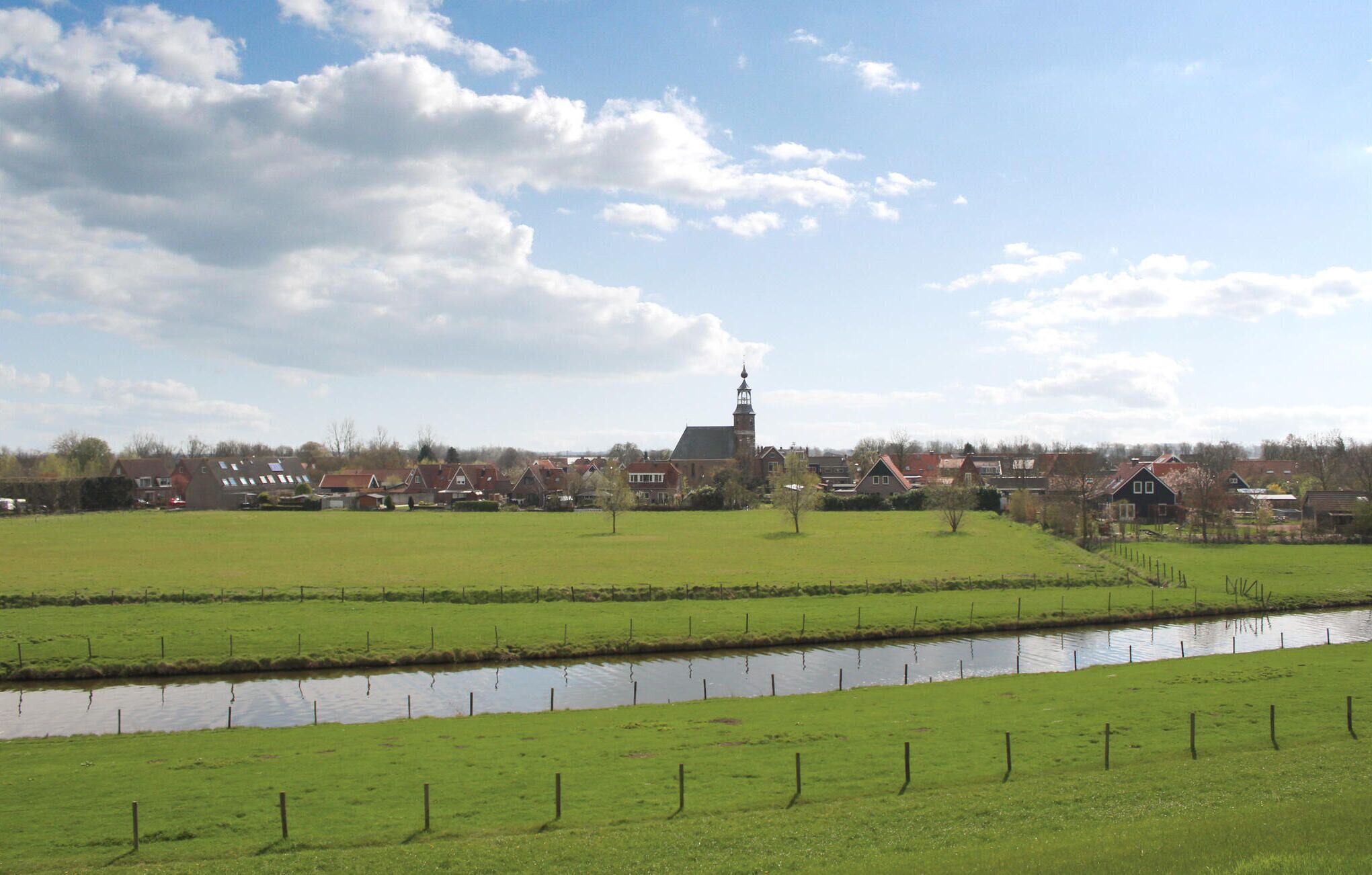 A rural landscape with a church, houses, and a canal.