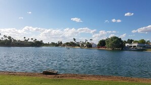 A lake with a boat, grassy areas, and buildings in the background. - Waterfront 1st Floor, Gated, 2 Bd,2Ba + Den, Family Friendly, Pet Friendly. (Scottsdale)