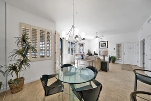 Un espace repas moderne avec une table en verre et des chaises noires, une plante en pot et un ventilateur de plafond.