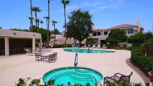 A pool area with lounge chairs and a covered seating area, surrounded by palm trees and a building with a red roof. - Waterfront 1st Floor, Gated, 2 Bd,2Ba + Den, Family Friendly, Pet Friendly. (Scottsdale)