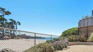 A fenced outdoor area with a view of the sea, a wooden building, and some vegetation. - Bay Watch Beach House (Santa Cruz)
