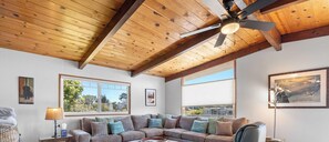 A living room with a wooden ceiling, a sofa, a lamp, and a window with a view. - Bay Watch Beach House (Santa Cruz)