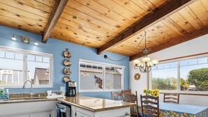 A kitchen with a wooden ceiling, a window with a view, and a table with a blue tablecloth. - Bay Watch Beach House (Santa Cruz)