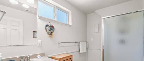 A bathroom with a shower, a towel rack, a window, and a decorative welcome sign.