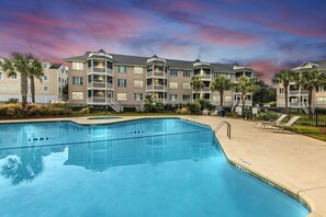 A swimming pool with a reflection of a multi-story building, palm trees, and a sunset sky. - End Unit Oceanfront Condo w/ Views from all Rooms (Isle of Palms)
