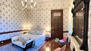 Un dormitorio con una cama grande, un sillón, una mesita con una taza y un platillo, y una chimenea.