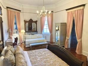 Ein Schlafzimmer mit einem großen Bett, einer Bank, einem Schminktisch, einem Spiegel und einer Chandelier.