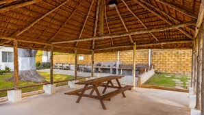 An outdoor pavilion with a thatched roof, picnic tables, and a brick wall. - Jobos Beach Apartment A-3 (Isabela)