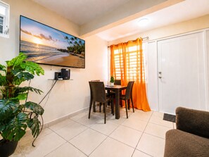 Uma área de refeições com mesa e cadeiras, uma televisão na parede e um vaso com planta.