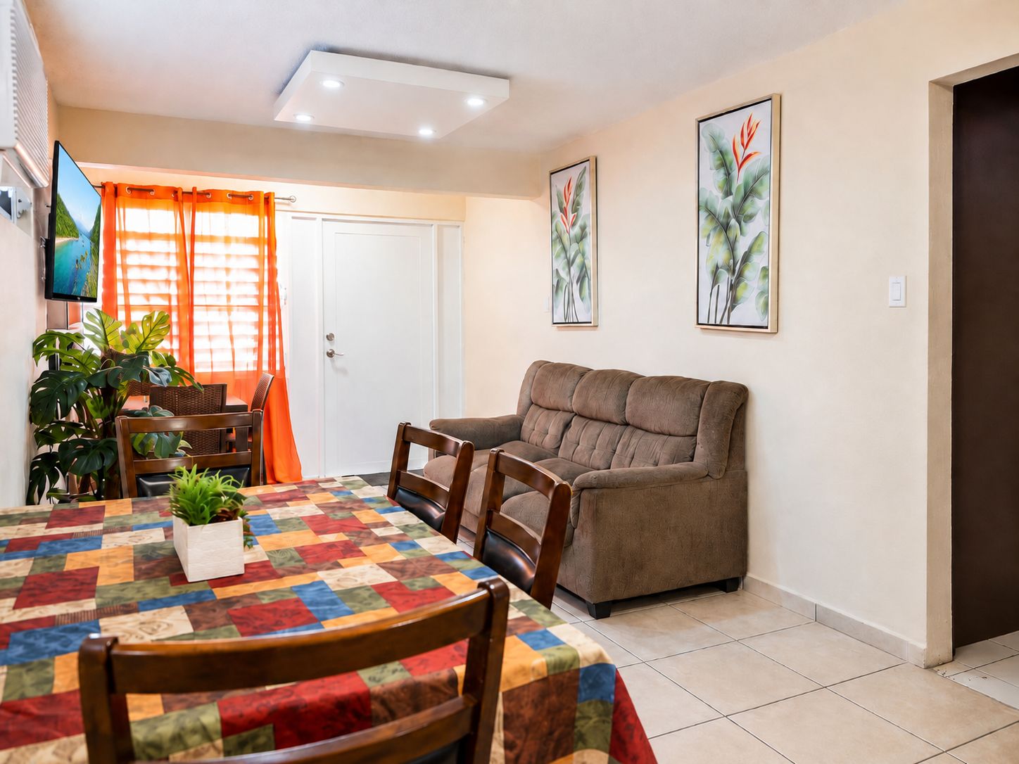 Una sala de estar con sofá, una mesa de comedor con sillas, un televisor y una puerta con cortinas.