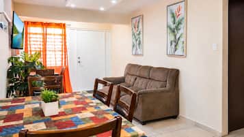 Una sala de estar con sofá, una mesa de comedor con sillas, un televisor y una puerta con cortinas.
