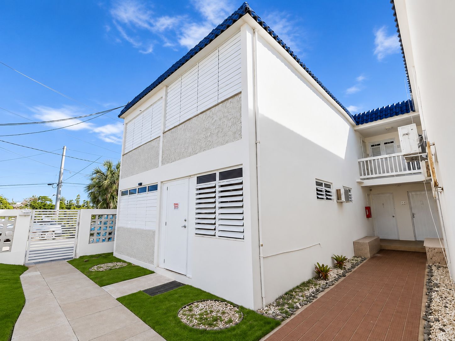 Un edificio residencial de dos pisos con balcón, puerta de garaje y un pequeño jardín.