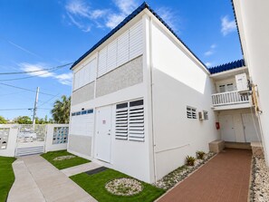 Um edifício residencial de dois andares com varanda, porta de garagem e um pequeno jardim.