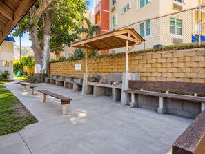 An outdoor seating area with concrete benches and a wooden pergola, surrounded by a brick wall and a tree. - Jobos Beach Apartment A-3 (Isabela)