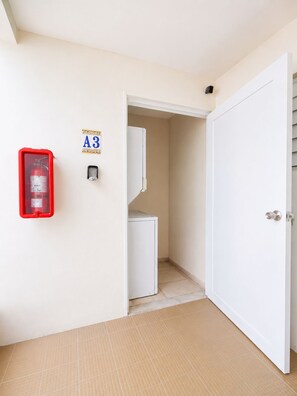A hallway with a white door, a red fire extinguisher, and a small refrigerator. - Jobos Beach Apartment A-3 (Isabela)