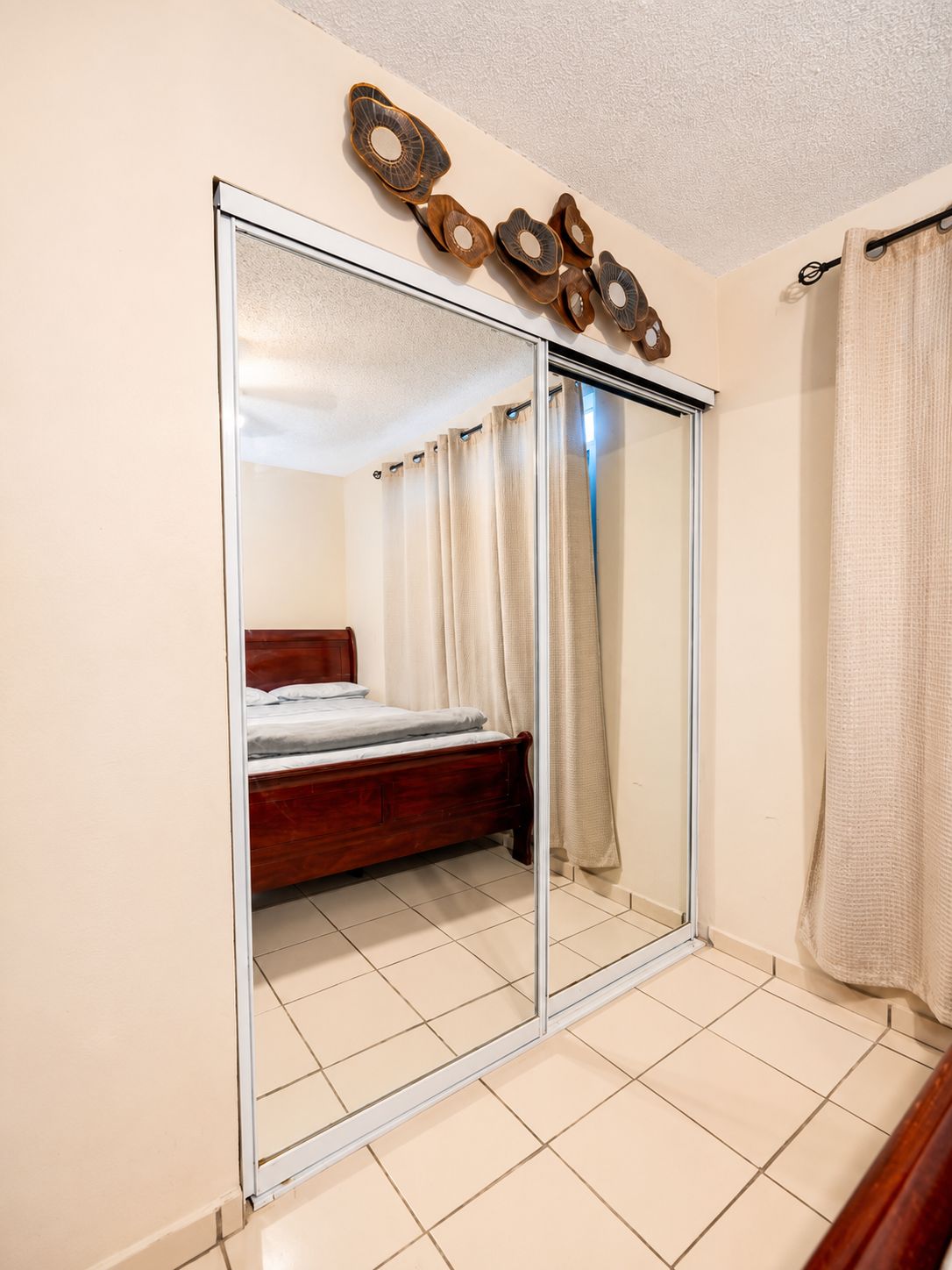 Un dormitorio con puerta corrediza de vidrio, una cama de madera y suelo de baldosas.