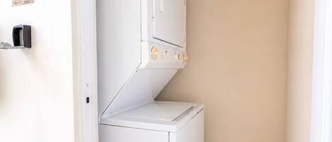 A compact, white laundry room with a single washer and dryer, a door with a sign reading 'A3', and a tiled floor.