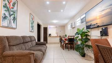 A living room with a sofa, a dining area with chairs and a table, and a kitchen in the background.