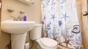 A bathroom with a white sink, toilet, and a shower curtain with sea creature designs. - Jobos Beach Apartment A-3 (Isabela)