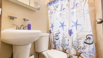 Un baño con lavamanos blanco, inodoro y cortina de ducha con motivos de criaturas marinas.