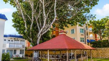 A gazebo with a red roof, surrounded by well-maintained grass, under a large tree.