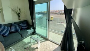 Un salon moderne avec un balcon en verre donnant sur une plage et l’océan.