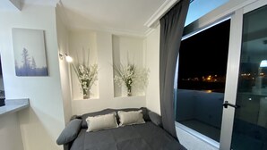 Une chambre à coucher avec un lit, une fenêtre avec des rideaux, une petite table et un tableau accroché au mur.