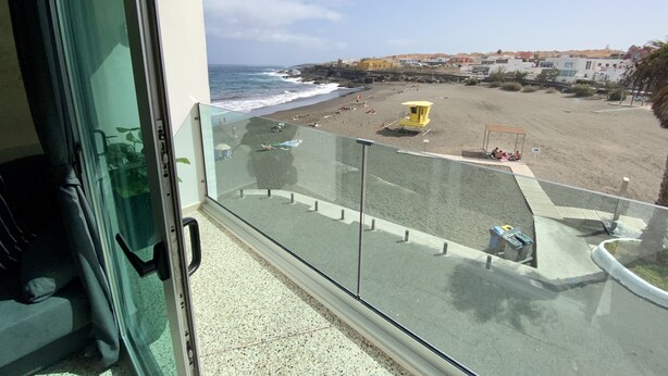 Un balcon donnant sur une plage, une tour de surveillance des sauveteurs et des bâtiments en arrière-plan.