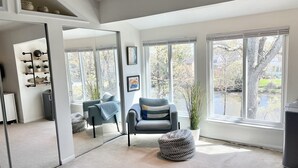 A modern living room with a large mirror, a grey armchair, a small round ottoman, and a bookshelf with decorative items. - UPDATED IN 2022  @Oceanfront - 3 Blocks 2Beach! 2 Suites 2.5 bath - great deck! (Virginia Beach)