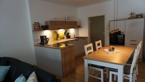 Une cuisine compacte dotée d’un îlot central en bois, de meubles blancs et d’un coin repas avec une table et des chaises en bois.