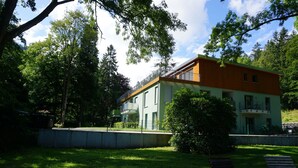Un bâtiment moderne à deux étages, doté d’un toit plat, entouré d’une végétation luxuriante et d’arbres.