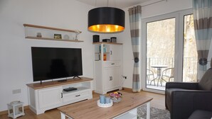 Un salon doté d’un téléviseur à écran plat, de meubles blancs, d’une table basse en bois et d’un balcon avec vue.