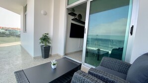 Uma varanda com mesa e cadeiras, um vaso de planta e uma televisão na parede.