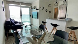 Uma sala de estar moderna com uma mesa de centro de vidro, um sofá e uma TV fixada na parede.