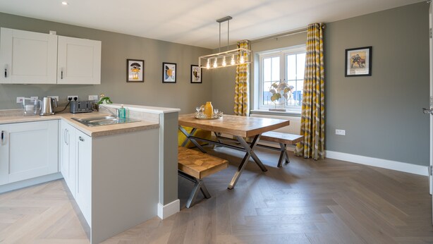 A modern kitchen with white cabinets, a wooden dining table, and a pendant light. - 6 Bedroom New Build Detached House in Bicester (Bicester)