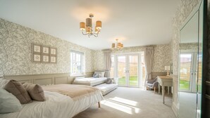 A bedroom with a large bed, a desk, and a chair. There is a window and a door leading to a balcony. - 6 Bedroom New Build Detached House in Bicester (Bicester)