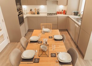 A modern kitchen with a dining table set for four, equipped with basic amenities like a stove, sink, and cabinets. - Stylish Chilterns Hills Escape | Walks & Parking (High Wycombe)