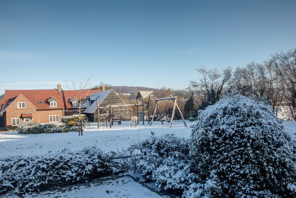 A residential area with a house, a wooden play structure, and snow-covered bushes. - Stylish Chilterns Hills Escape | Walks & Parking (High Wycombe)