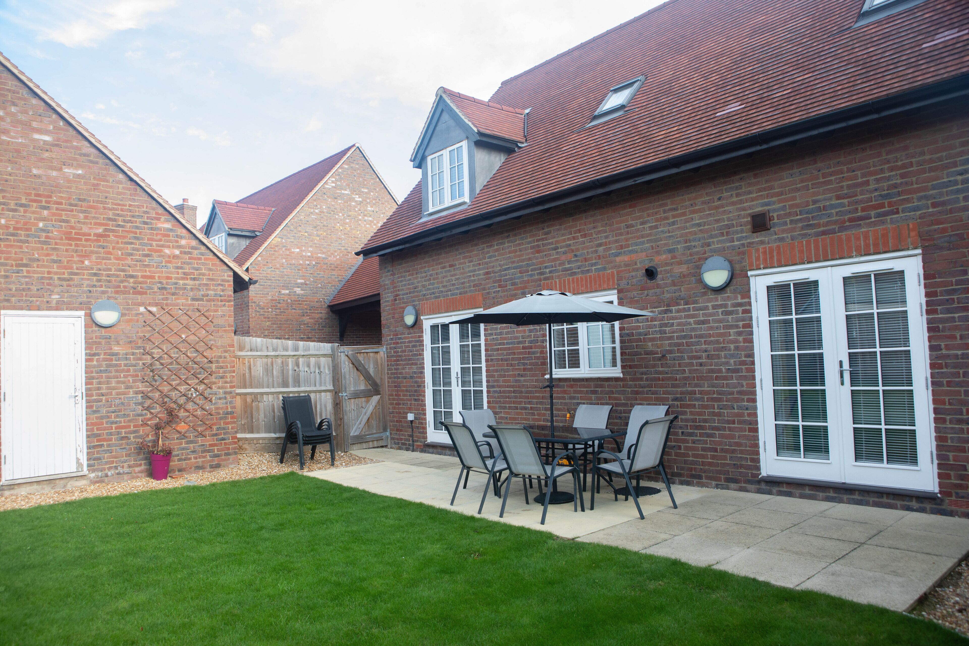 A brick house with a patio area featuring a table and chairs, a potted plant, and a wooden fence.