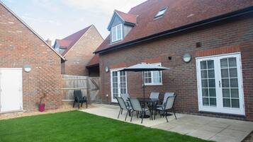 A brick house with a patio area featuring a table and chairs, a potted plant, and a wooden fence.