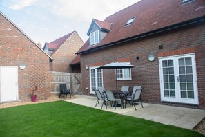 A brick house with a patio area featuring a table and chairs, a potted plant, and a wooden fence. - Stylish Chilterns Hills Escape | Walks & Parking (High Wycombe)